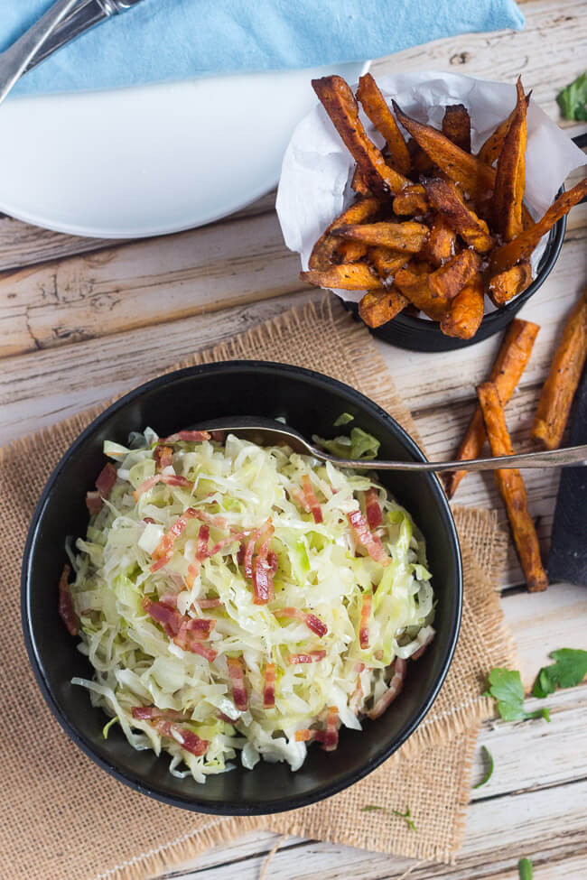 Overhead shot of a bowl of fried cabbage with bacon, and a basket of crispy sweet potato chips.