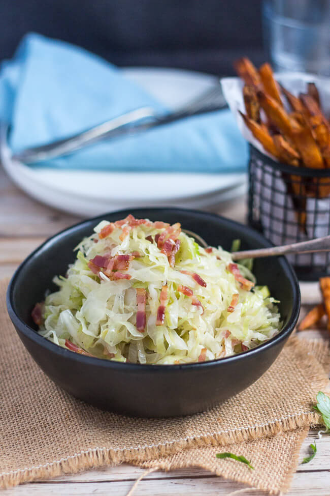 A bowl of fried cabbage with bacom, and a basket of crispy sweet potato chips in the background.  