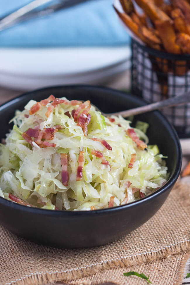 A small black bowl full of fried cabbage with bacon.