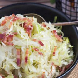 A close up shot of fried cabbage with bacon in a black bowl.