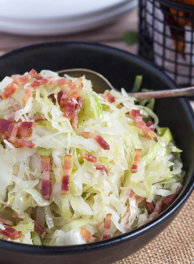 A close up shot of fried cabbage with bacon in a black bowl.