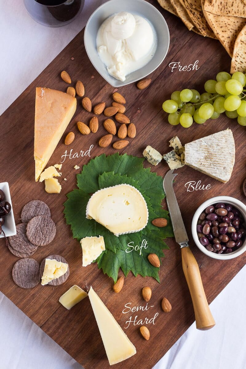 An overead shot of a jarrah cheese platter, with a selection of different cheeses, grapes, nuts, olives and crackers.