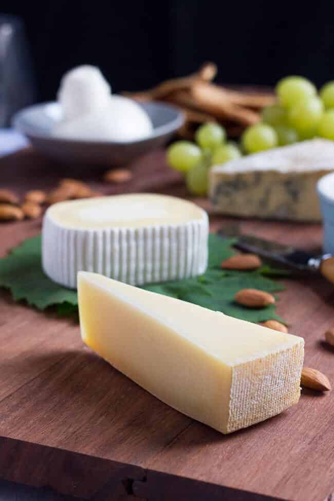 A wedge of Tilsit cheese sitting on a jarrah cheese platter, with a soft cheese, fresh burrata and blue cheese in the background.