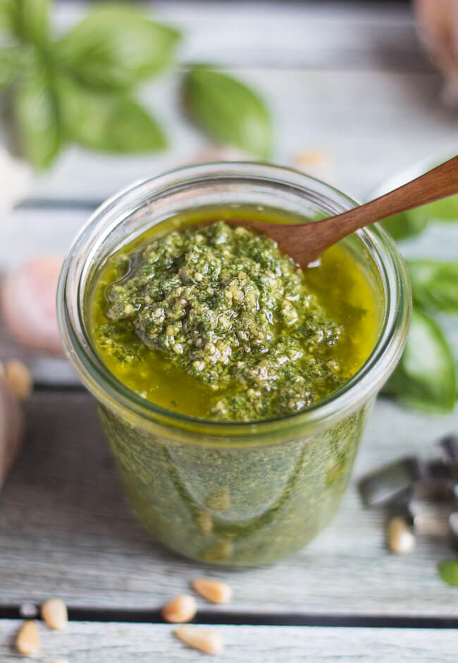 A jar of basil pesto sauce, with a wooden spoon dipped into it.