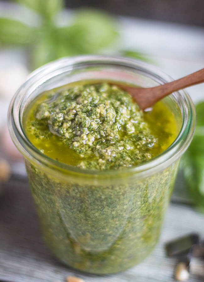 A jar of freshly made basil pesto sauce, with free olive oil on top.