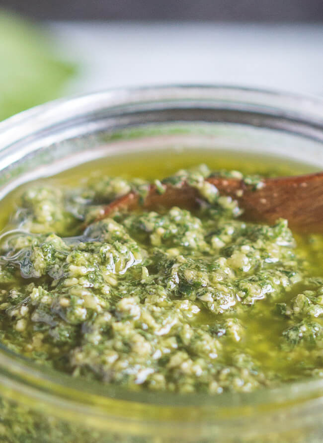 A close up shot of a jar of basil pesto sauce, showing the consistency of the freshly made pesto. 