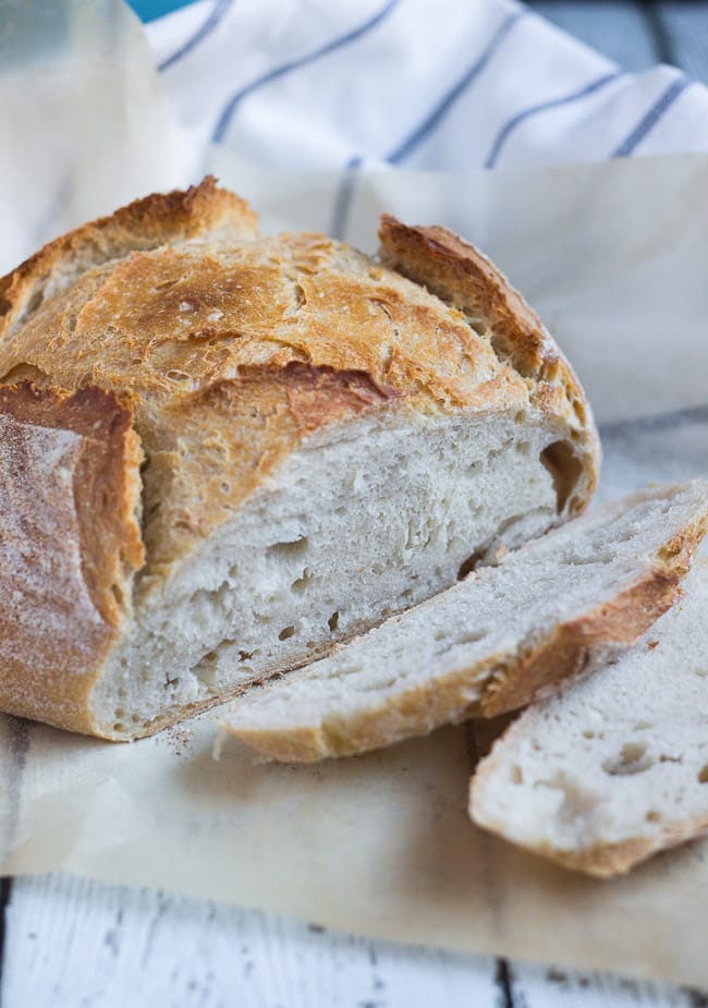 A loaf of cooked 5 minute artisan bread.  Two slices of bread cut from the loaf lie to the right of the intact loaf.  