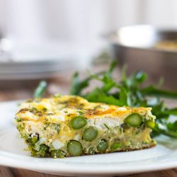 A slice of asparagus and goat cheese frittata on a white plate.