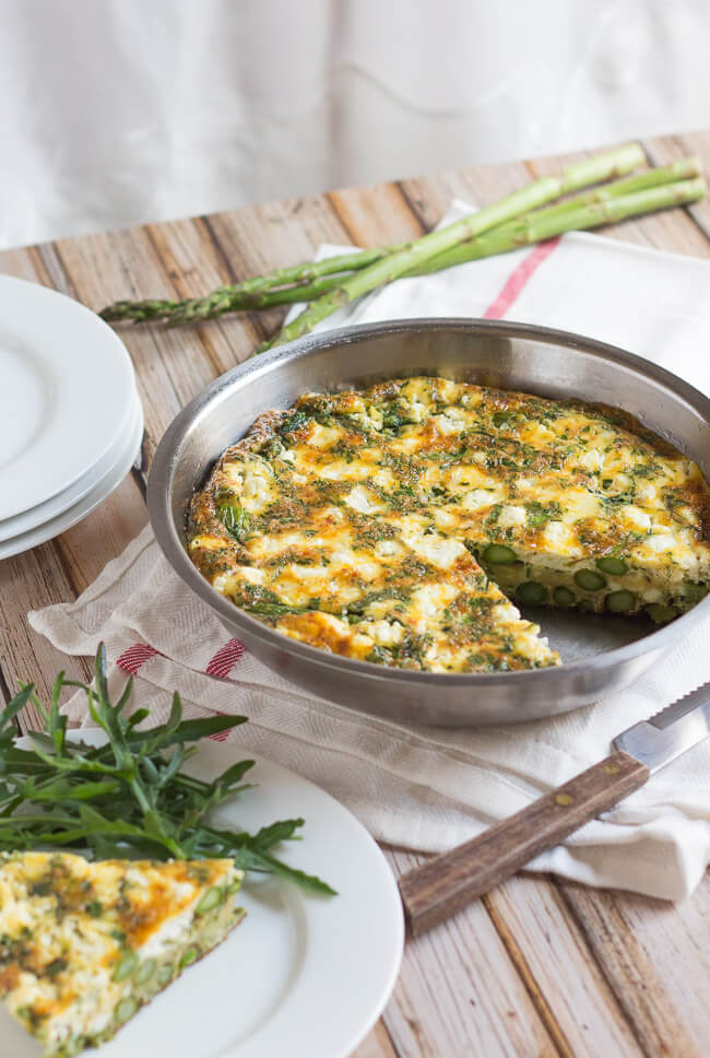 Asparagus & goat cheese frittata in a stainless steel fry pan, with a slice removed.