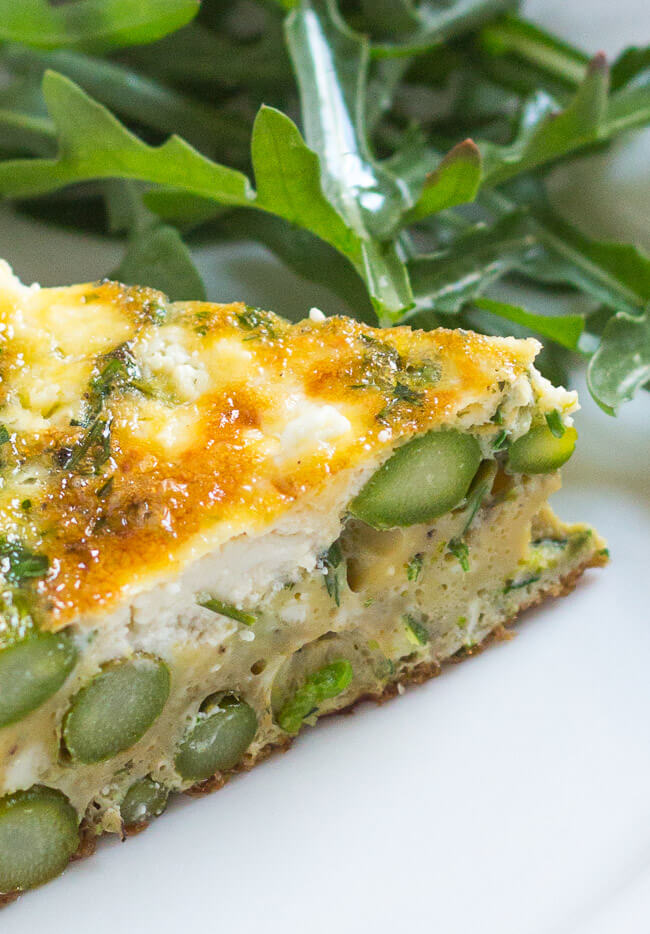 A close up shot of a slice of asparagus & goat cheese frittata on a white plate. 