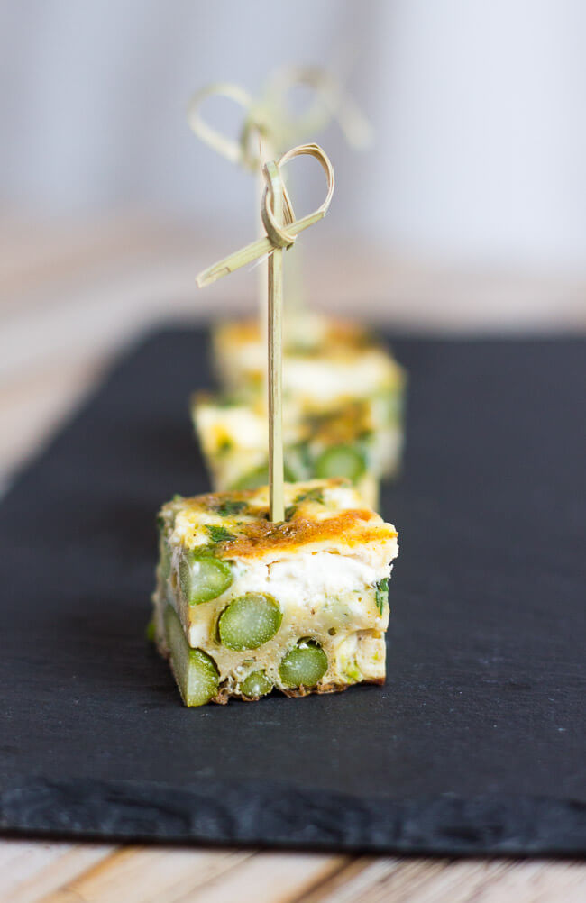 Cubes of asparagus & goat cheese frittata on a toothpick, arranged on a slate tile. 