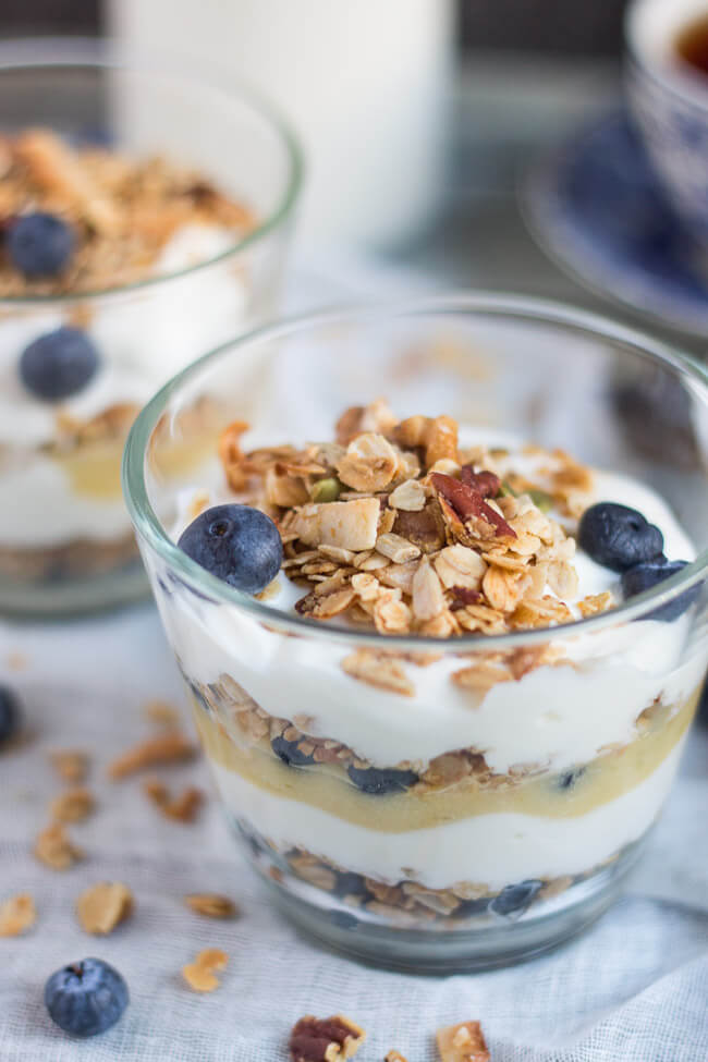 Layered blueberry lime curd breakfast parfait in a glass, with granola and blueberries on top.