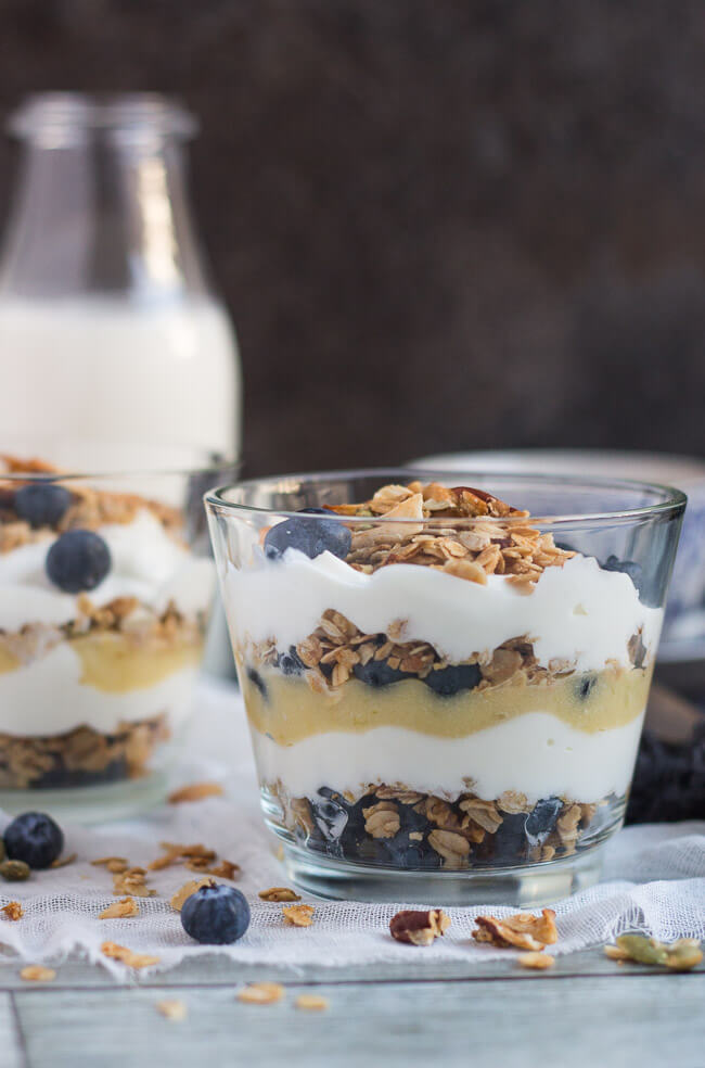 Two blueberry lime curd breakfast parfaits in a glass, with a bottle of milk in the background.