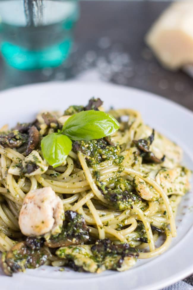 A grey plate filled with Chicken Pesto Pasta with Mushrooms with a fresh basil leaf on top. 