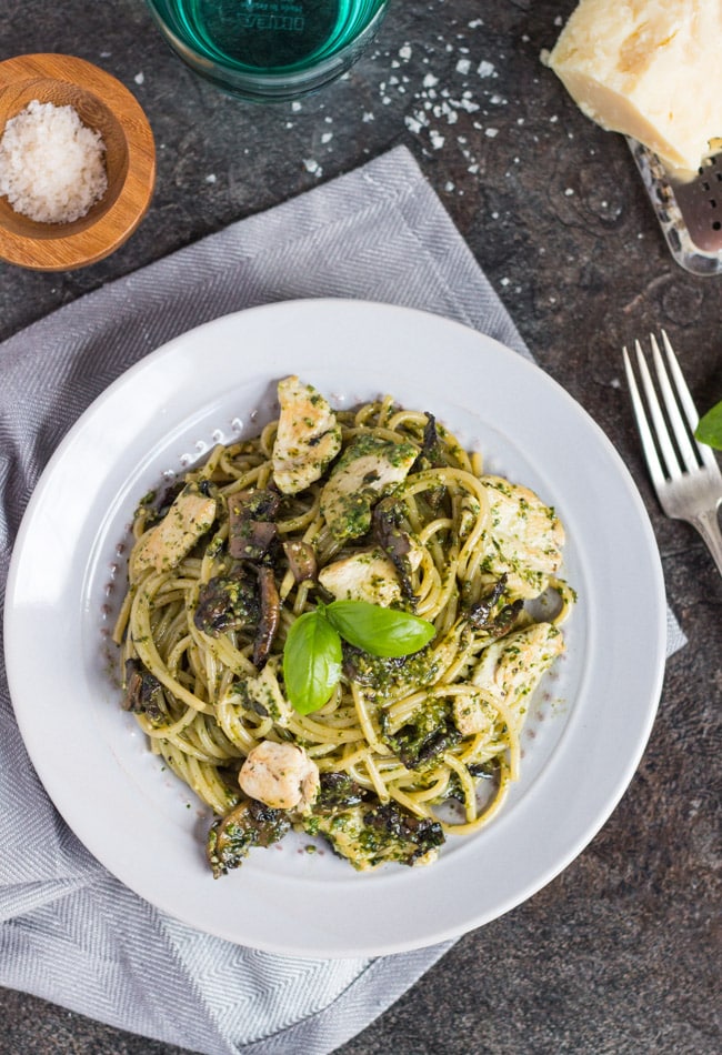 Overhead view of a grey plate on a grey napkin.  A pile of pesto pasta with pieces of chicken and mushroom sits on the plate.  