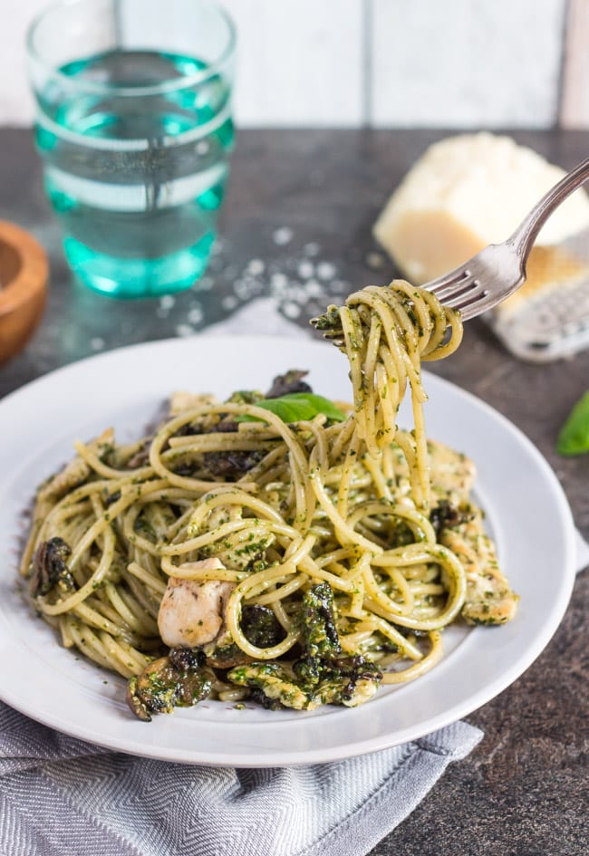 Pesto coated spaghetti twirled around a fork hovers over a plate of chicken pesto pasta.  