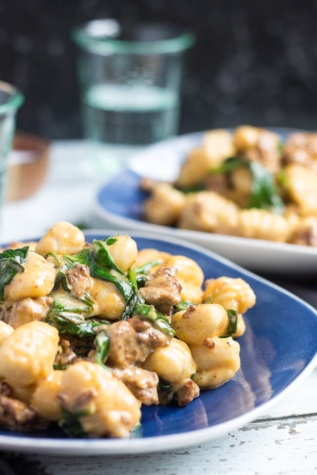 A blue plate, piled high with a chorizo & creamy spinach easy gnocchi recipe. A second plate can be seen in the background. 