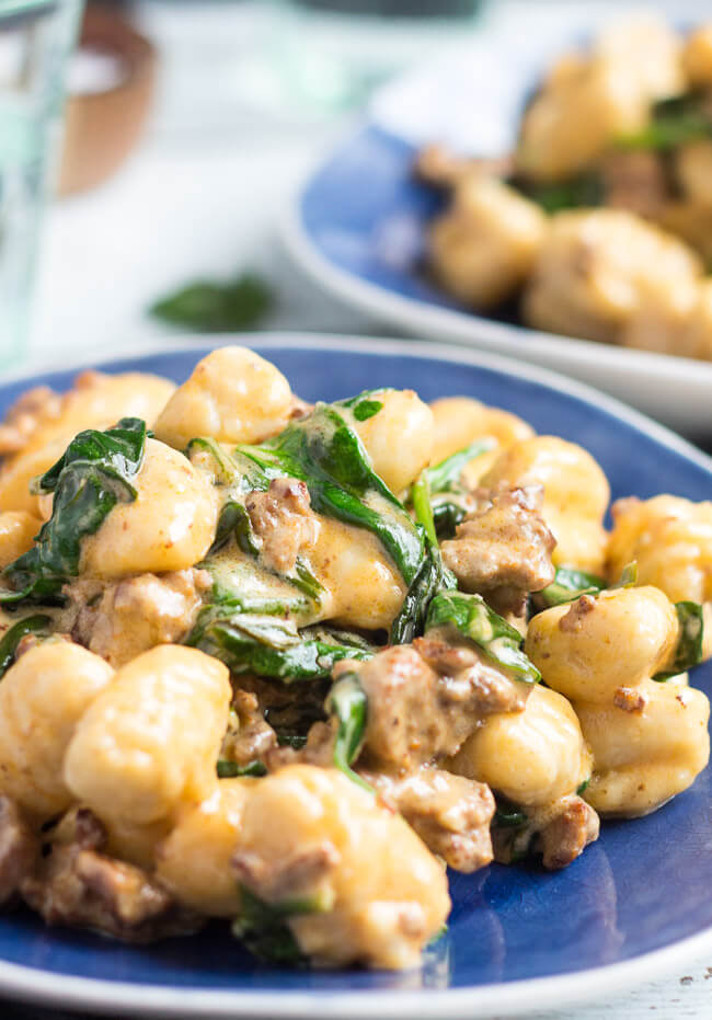 A shot of chorizo & creamy spinach easy gnocchi recipe on a blue plate, with a green water glass in the background.  