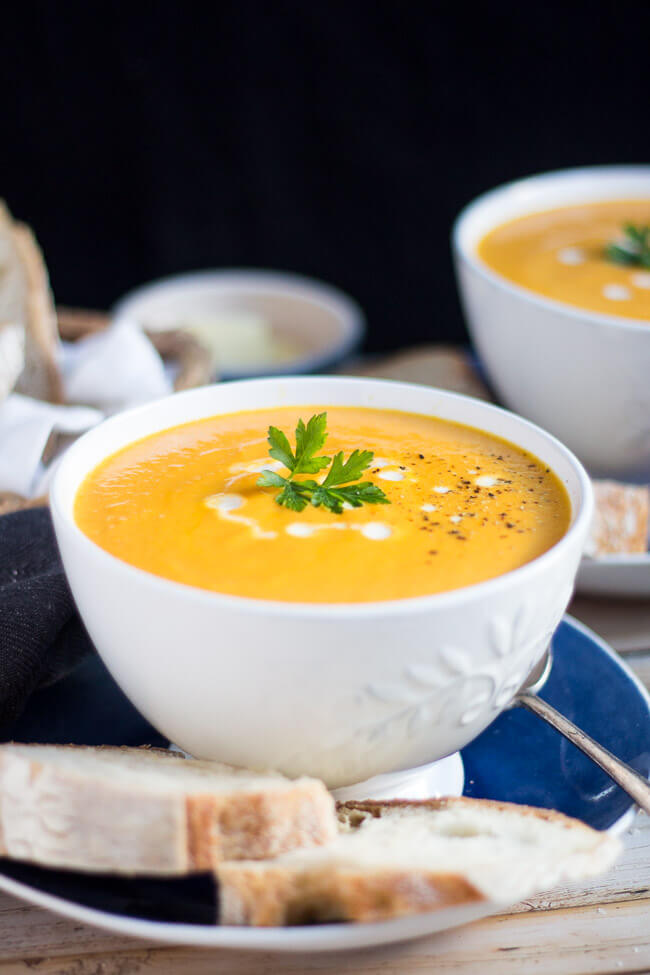 Two white bowls, full of creamy carrot soup accompanied by slices ofcrusty bread.