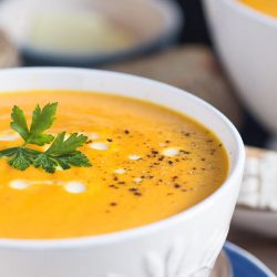 A close up of a white bowl full of creamy carrot soup.