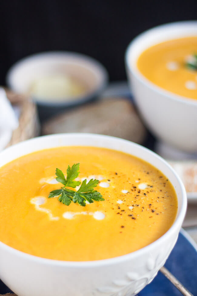 Two bowls of creamy carrot soup, drizzled with cream and a dusting of cracked black pepper.