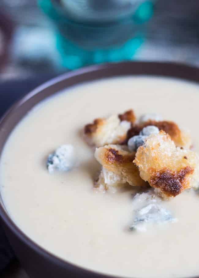 A close up shot of the top of the bowl of this easy cauliflower cheese soup recipe. Crumbles of blue cheese and crispy sourdough croutons sit on top of the soup. 