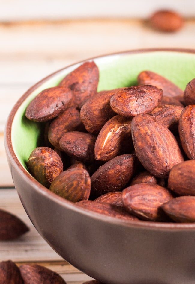 A close up shot of crispy tamari almonds sitting in a brown bowl with green insides.  