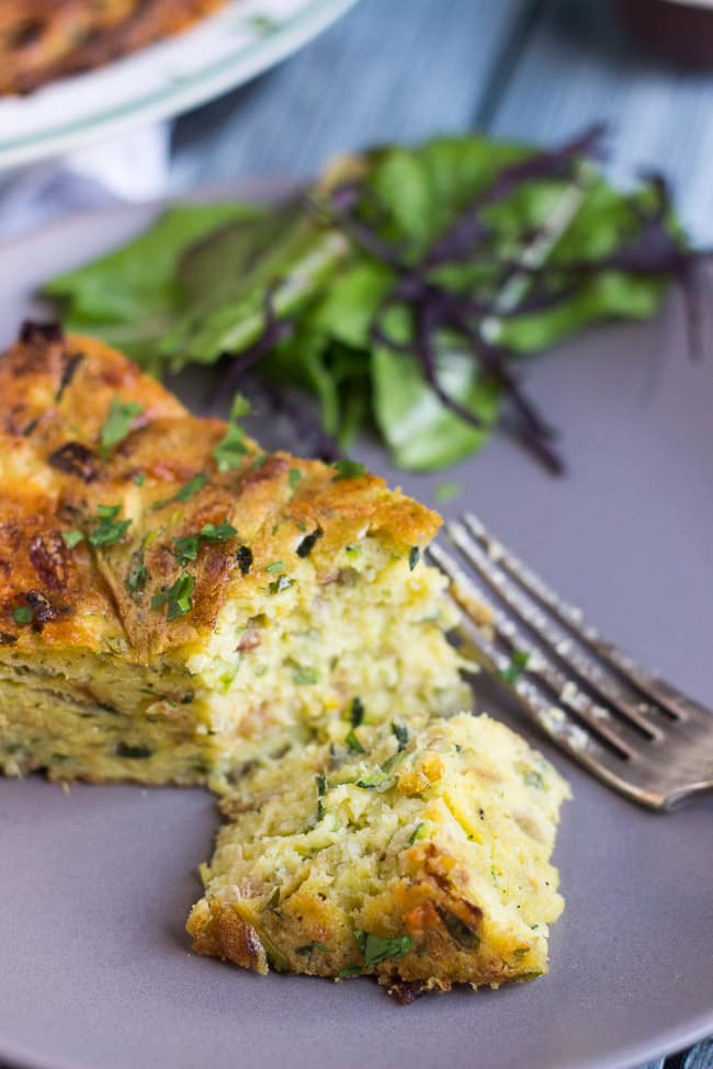 A slice of healthy crustless zucchini quiche with the tip sliced off.  The severed tip lies on its side with a silver fork next to it.  