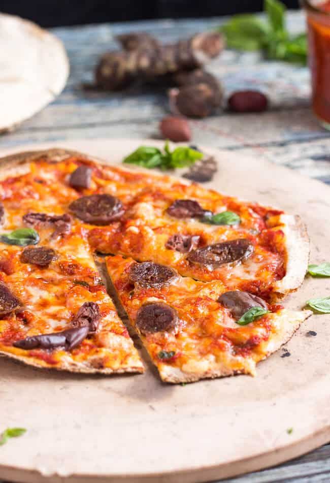 Cooked flatbread pizza recipe on a stone pizza slab, with a wedge of cut pizza showing.  