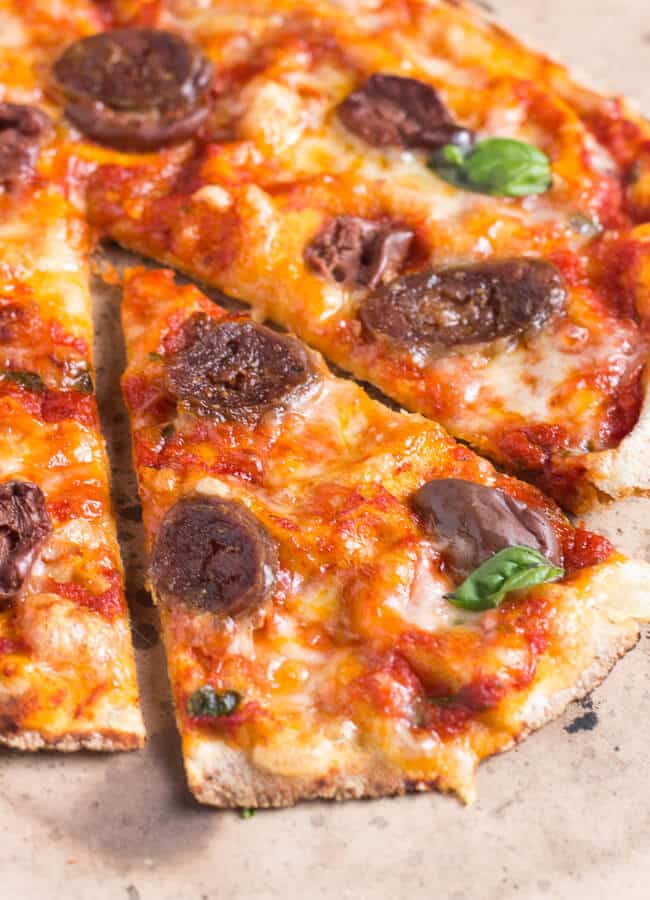 A close up shot of a wedge of pizza with a crusty tomato cheese base, and slices of salami and olives.  