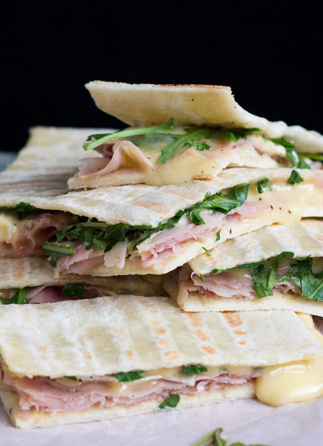 A pile of ham & brie flatbread sandwiches, with molten cheese oozing down the pile.