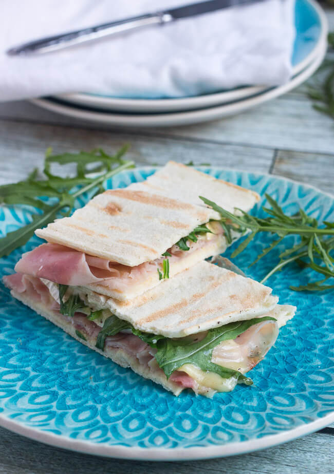 Two ham & brie flatbread sandwiches on a blue plate.