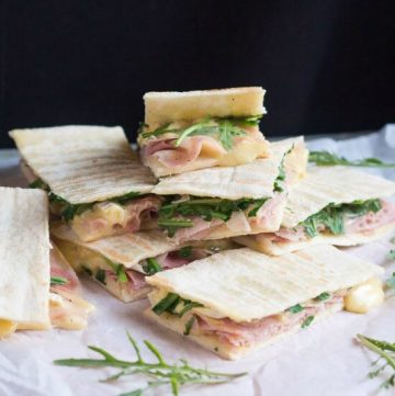 A pile of ham & brie flatbread sandwiches, with brie oozing from the sides.