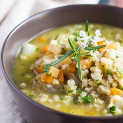 A brown bowl full of hearty Winter Vegetable Soup. Swollen grains of barley and small cubes of winter vegetables are visible in the soup.