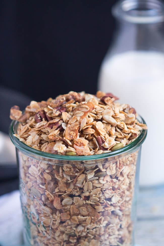 A weck jar full of a simple homemade crunchy granola recipe, with a glass bottle of milk in the background.