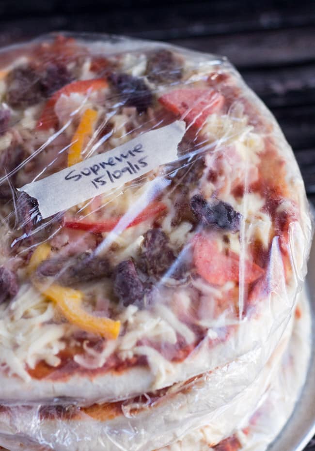 A pile of homemade pizzas, wrapped in plastic and labelled, ready for the freezer. 