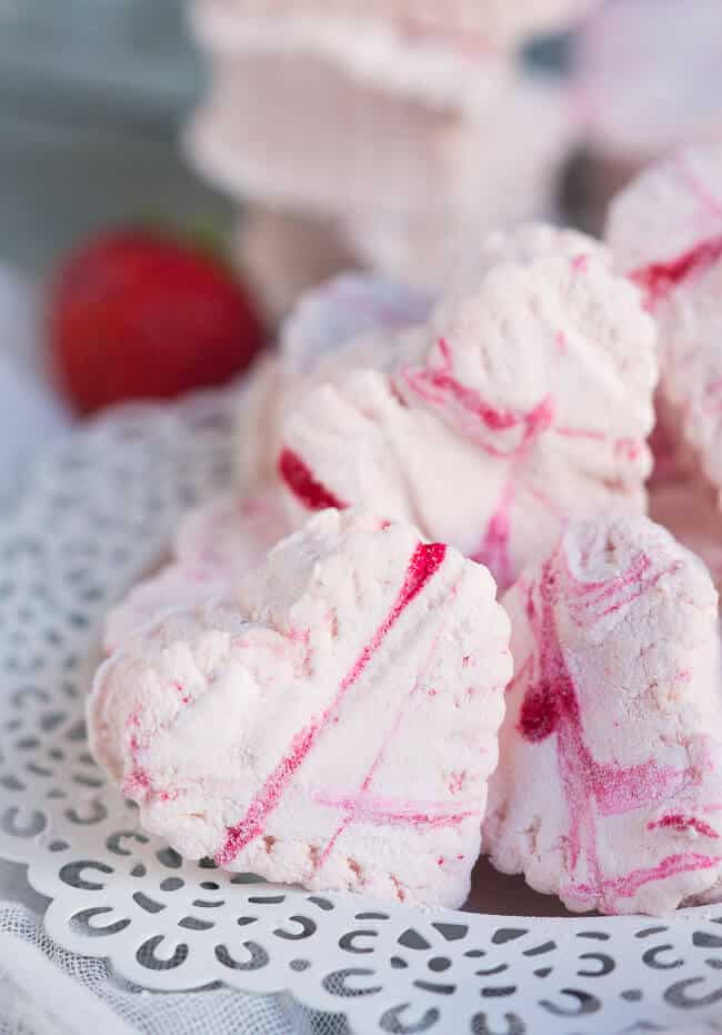 Three pink heart-shaped homemade strawberry marshmallows on a white plate with a lattice edge. 
