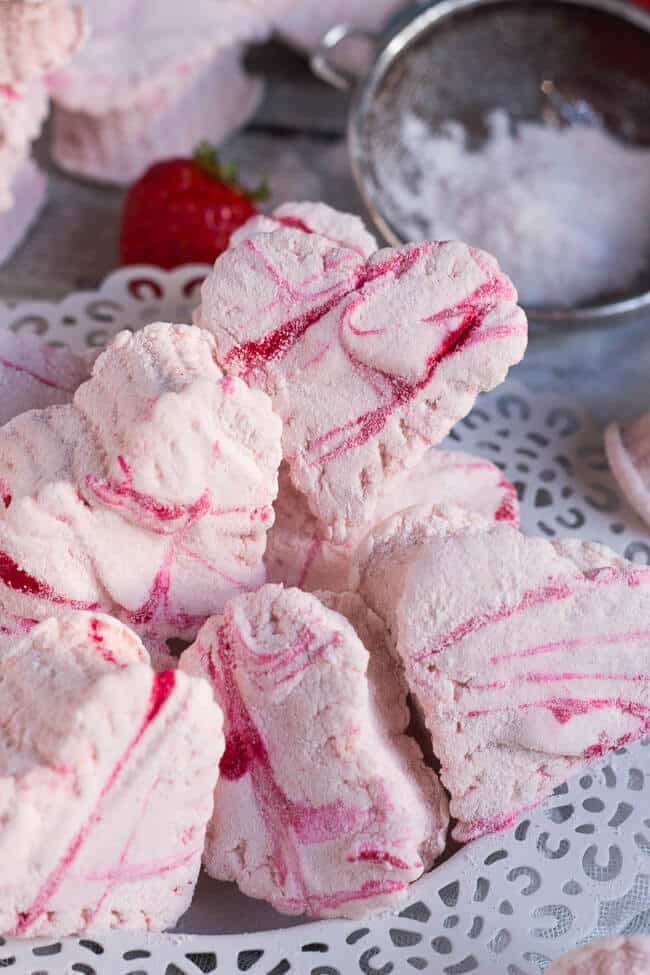 A pile of pink homemade strawberry marshmallows on a small white plate with lattice edge. 