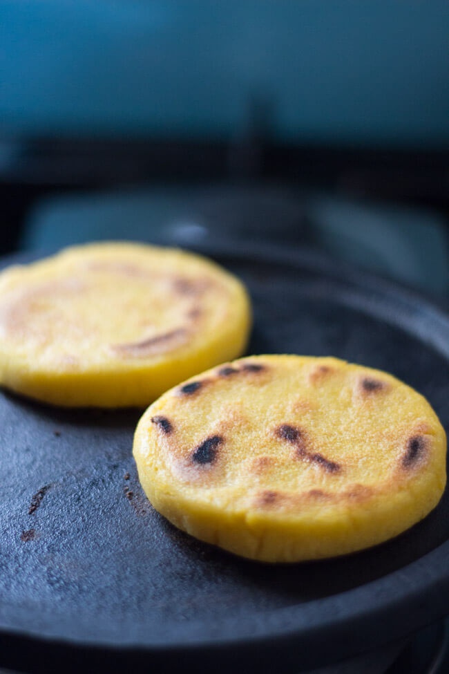 How To Make Arepas: Two arepas cooking on a Mexican comal. 