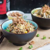 A brown bowl, with blue interior, full of fried rice and scattered with crispy fried onions.