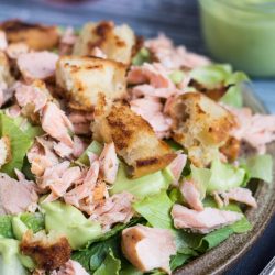 Flaked salmon and crispy homemade croutons on a bed of chopped Romaine lettuce, surrounded by blobs of creamy avocado dressing.