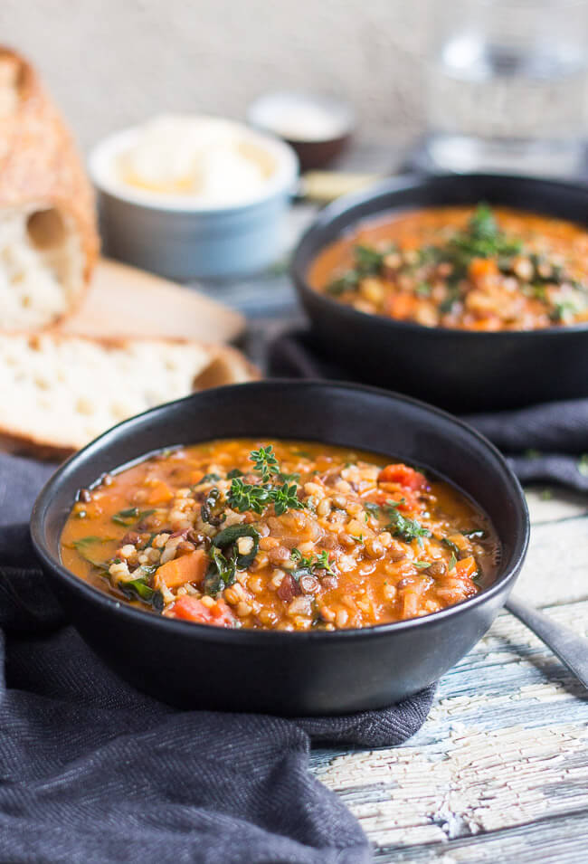 Two bowls of hearty lentil and brown rice soup recipe, with a loaf of bread and pot of butter in the background.