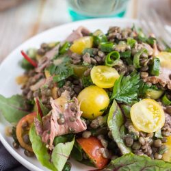 Cold roast beef salad recipe, with yellow tomatoes, beetroot leaves and green lentils on a white plate.