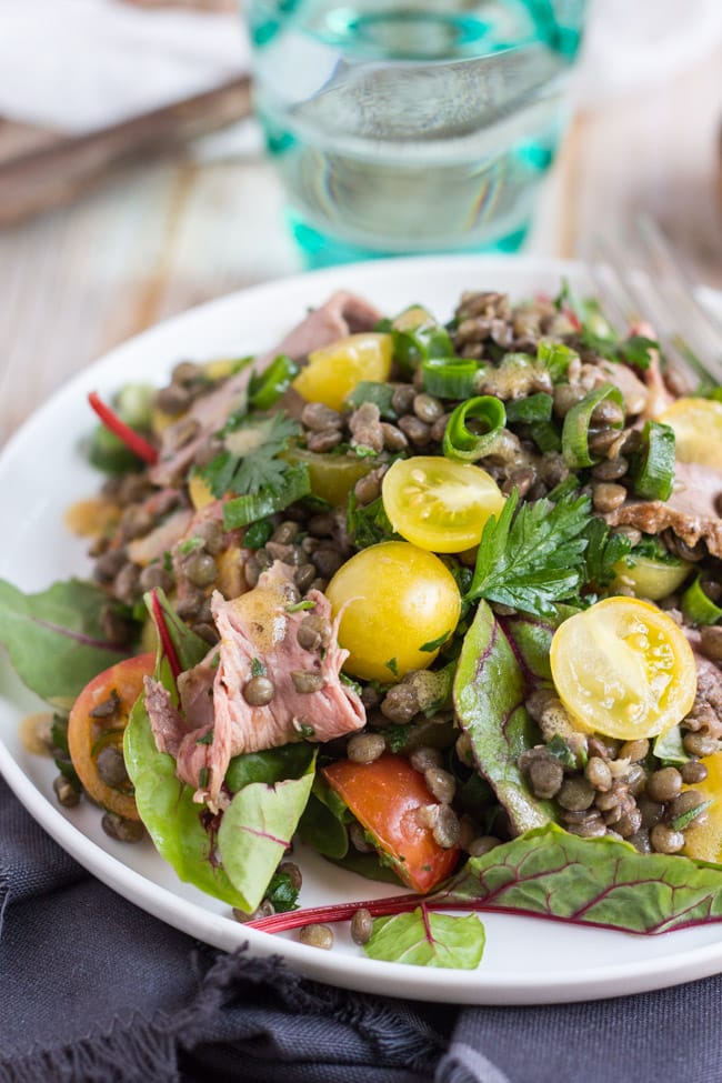 Cold roast beef salad recipe, with yellow tomatoes, beetroot leaves and green lentils on a white plate.  