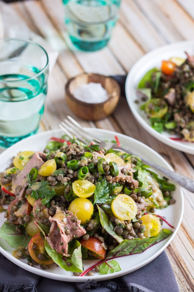 Cold roast beef salad, with shaved beef, green lentils and drizzled with mustard dressing, on a white plate.   