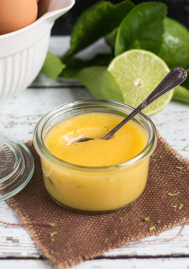 A pot of lime curd, with a jug of eggs and limes in the background.