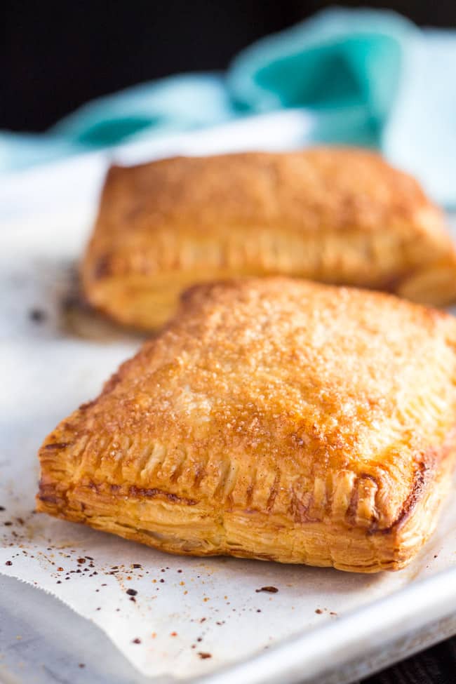 Two cooked apple turnovers, from an easy apple turnovers recipe, on a lined baking tray. 