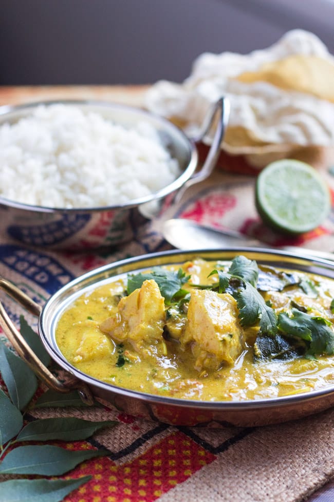 A copper bowl, filled with the best fish curry recipe.  A bowl of rice and a plate of pappadums sits in the background.