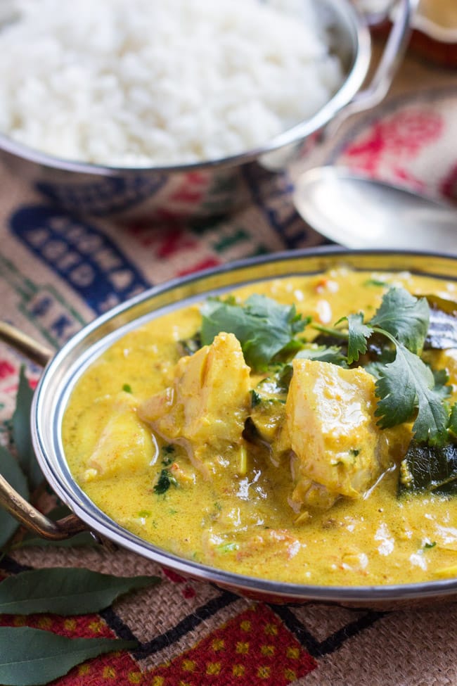 A close up shot of the fish chunks, surround by creamy yellow sauce, in a bowl of quick fish curry.  A bowl of rice sits in the background.  
