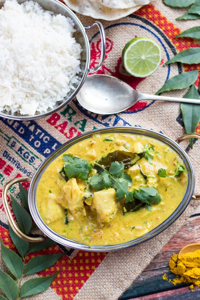 An overhead shot of a bowl of easy fish curry, accompanied by a bowl of rice and a cut lime.   